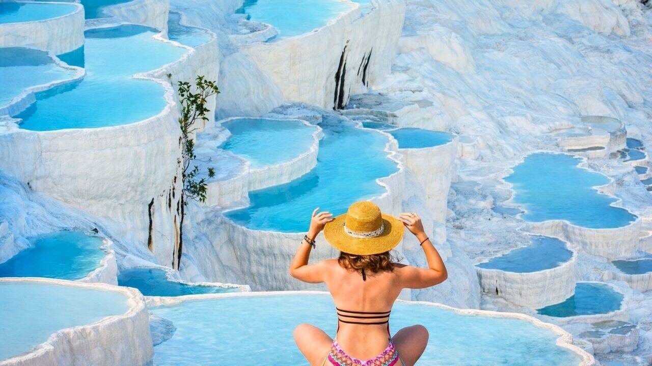 Visitors walking on the white travertine terraces filled with turquoise thermal water at Pamukkale